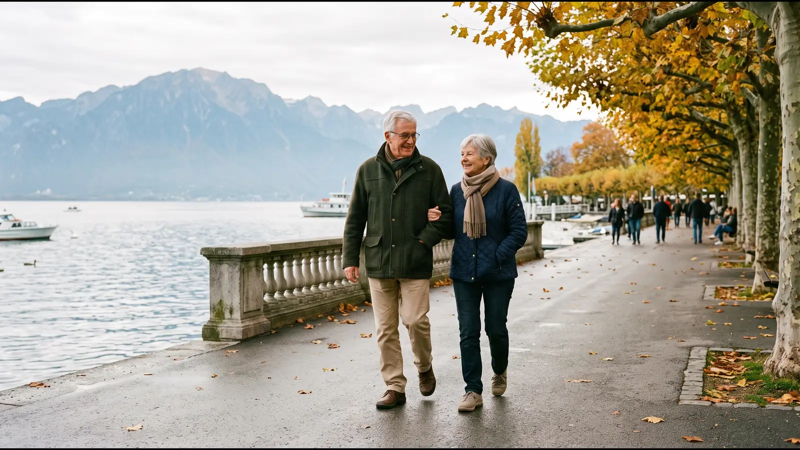 Un couple de retraités se promène bras dessus, bras dessous sur un quai au bord du Léman, en automne.
